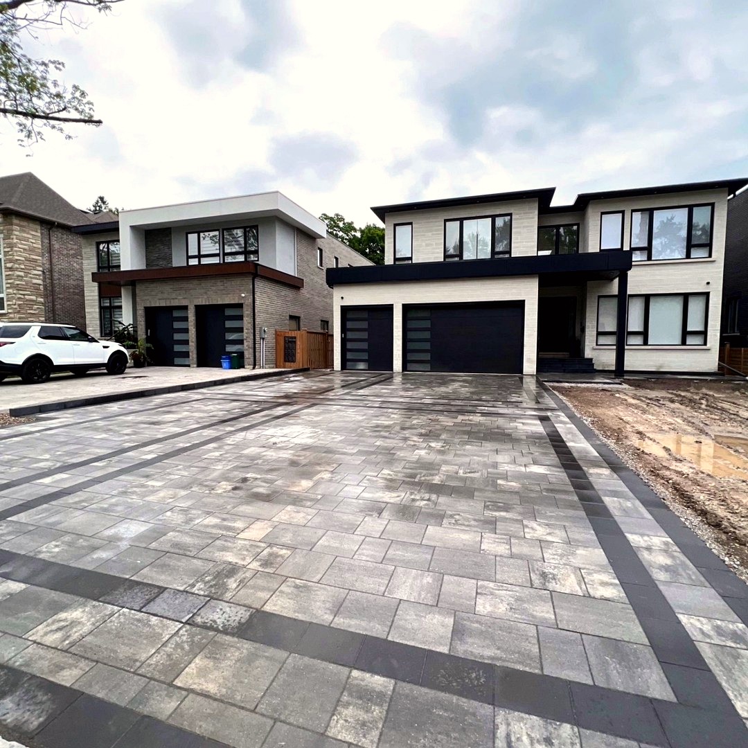 Large grey interlocking paver driveway with charcoal border in front of modern homes