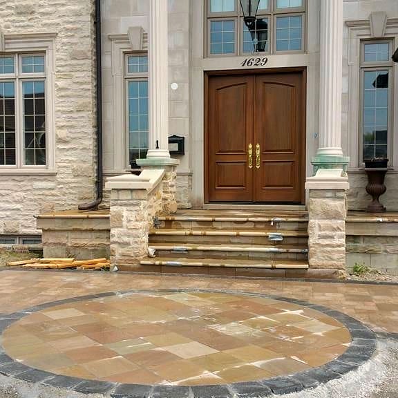 Stone veneer front entrance with double wood doors and circular paver medallion in Durham Region