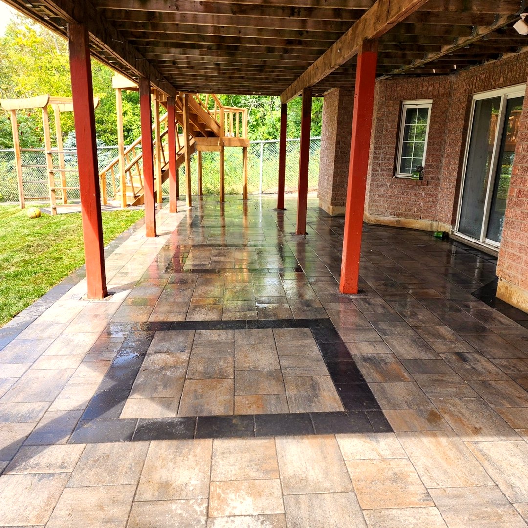 Glossy interlocking patio under a raised deck with accent inlay and steel posts